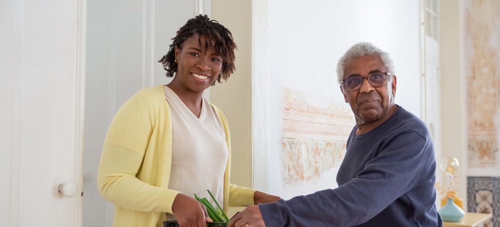 A neighbour handing a crate of groceries to an older man at his front door